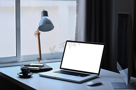 笔记本电脑配有平板屏幕、灯、咖啡杯和白色桌子上的书籍。
