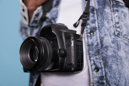 摄影爱好者穿着时尚牛仔夹克，同时拥有现代数码单反相机的特写镜头。