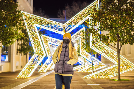 晚上，女孩戴上针对冠状病毒COVID 19的医用口罩，在装饰有节日灯光的圣诞传统市场上散步。