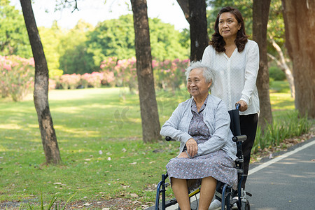 轮椅下坡摄影照片_护理人员帮助和护理亚洲老年或老年老妇患者坐在公园里的轮椅上，快乐地坐着，健康强大的医疗理念。