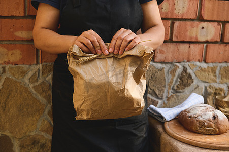 食品工人摄影照片_一位女面包师的剪影，一位工匠面包店工人拿着一个生态纸袋，里面装着新鲜的传统面包