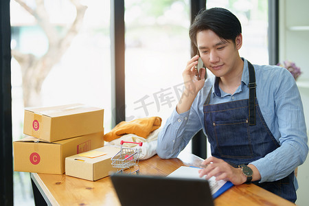 一家小型初创企业和中小企业主的肖像，一位亚洲男性企业家使用手机检查订单以整理产品，然后将其装入内盒供客户使用