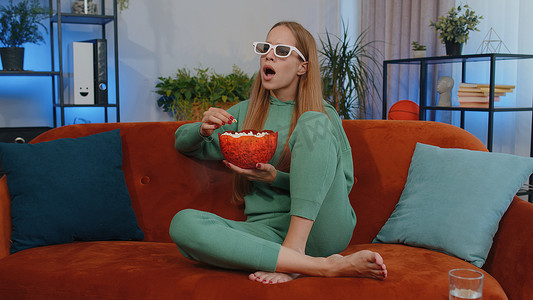 电影视频片摄影照片_女孩坐在沙发上吃爆米花，在家看有趣的电视连续剧、在线体育比赛