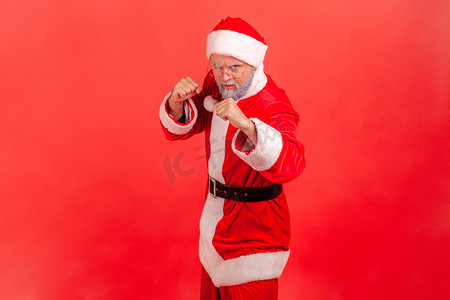 严格的老人，留着灰胡子，穿着圣诞老人服装，握着拳头站着，准备战斗，表情愤怒地看着镜头。