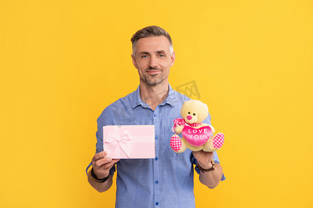 购物节购物节摄影照片_快乐的头发花白的家伙拿着黄色背景的盒子和玩具，爱