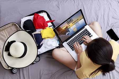 亚洲幸福女人的顶视图是通过笔记本电脑在家里的床上预订酒店来计划旅行。
