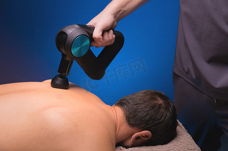 物理治疗师用按摩敲击装置治疗男性的脊柱和背部。
