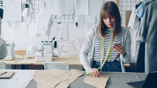 创意海报设计创意摄影照片_服装设计企业家正在检查纸质缝纫草稿并查看智能手机。