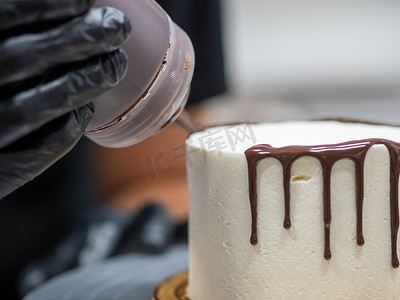 融化的巧克力滴摄影照片_蛋糕设计师用巧克力甘纳许滴釉，奶油白色光滑蛋糕