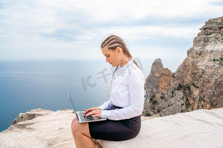 macbook摄影照片_一位女士坐在露台上用 MacBook 键盘打字，可以看到美丽的海景。