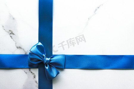 蓝色装饰彩带摄影照片_豪华大理石背景上的蓝色丝带和蝴蝶结、假日平底背景