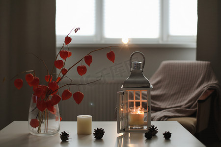 橙色家居摄影照片_舒适的秋季静物、蜡烛、鲜花、花瓶中的橙色酸浆树枝以及家居室内的细节