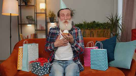 快乐的老人庆祝生日聚会，许愿在小纸杯蛋糕上吹蜡烛
