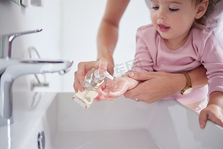 幼儿在水槽里弄脏手指后，母亲用消毒液肥皂清洁孩子的双手。