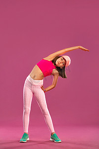 粉色背景活动摄影照片_小女孩穿着运动服在粉色和粉色背景下进行健身锻炼。