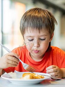 红色叉摄影照片_穿红色T恤的小孩用刀叉吃煎饼。