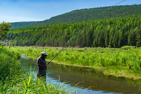 一位渔夫站在河里，用一根木鱼竿钓鱼。