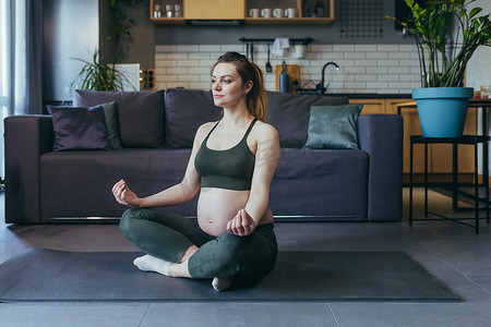 美女莲花摄影照片_怀孕的美女在家做瑜伽，坐在莲花位置的运动垫上