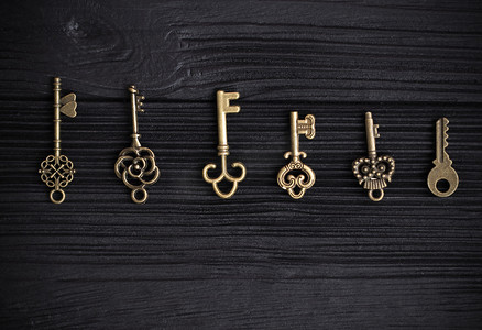 一套古董铜钥匙排成一排，位于黑色木质背景上。