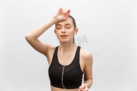 疲惫的健身女人在艰苦的训练后出汗，在电话里听音乐休息一下。