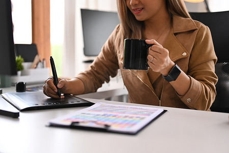 使用图形平板电脑微笑的年轻女性在当代工作场所从事新创意项目的裁剪镜头