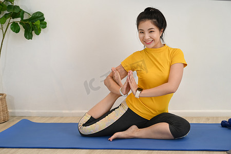 健身教练摄影照片_年轻健康的女性在家里的垫子上练习瑜伽。