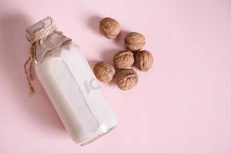 饮料瓶摄影照片_平躺瓶，配有健康植物牛奶和核桃，粉红色背景，带复制空间。