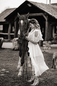 美丽的女孩穿着白色的太阳裙，旁边是一个老牧场的一匹马。