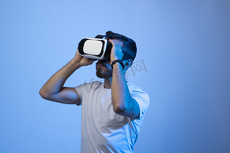 虚拟现实现实摄影照片_留着胡须的年轻人使用 VR 眼镜，用手触摸复制空间自由空间，与朋友在线玩虚拟视频游戏。