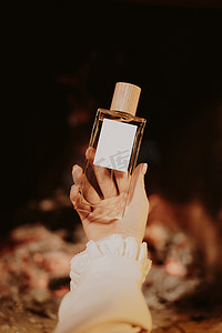 美丽的简约香水瓶在女性手中，在壁炉火焰背景上。