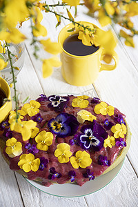 白色木桌上用黄紫色三色堇花装饰的美味蛋糕