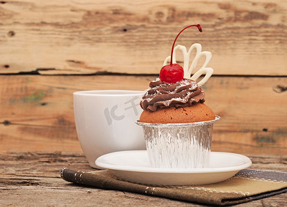 老木背景上有巧克力奶油和樱桃的纸杯蛋糕