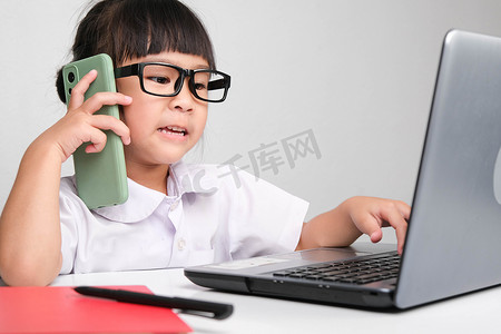 儿童自信摄影照片_带着笔记本电脑在办公室工作、打电话的小女商人 儿童和商业概念