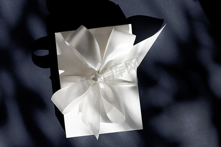 装饰礼物盒摄影照片_黑色背景上带丝带和蝴蝶结的豪华假日白色礼盒、豪华婚礼或生日礼物