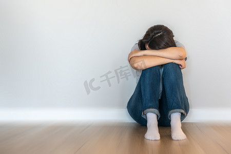 悲伤的女人摄影照片_悲伤的女人独自坐在空荡荡的房间里的地板上，绝望和孤独的概念与运动模糊效果