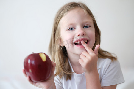 人类手臂摄影照片_手里拿着红咬苹果的无牙微笑可爱女孩的肖像