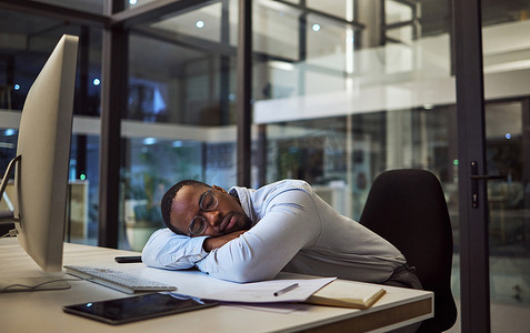 夜间营业、工作睡眠和商人在一家公司的黑暗办公室里睡在办公桌上，电脑上。