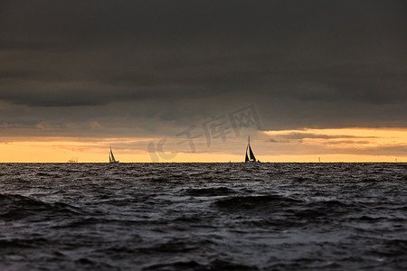 海上暴风雨摄影照片_帆船在海上暴风雨天气，风雨如磐的云天橙色天空，风帆赛船会，风帆在水中的反射，大水波，