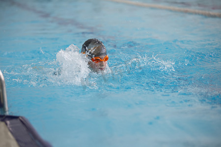 一个戴着泳帽和眼镜的男孩正在运动池里游泳。