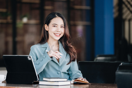 一位女性企业家或女商人在阅读一本制定金融和投资策略的书并在木桌上操作平板电脑时露出微笑。