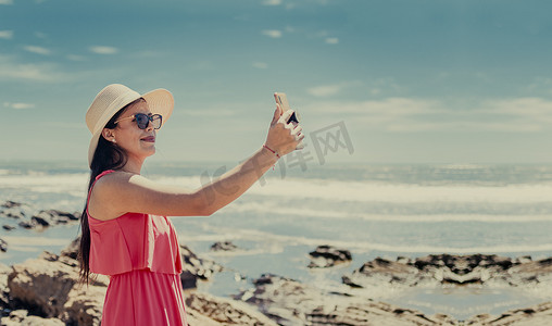 帽子女人在海上拍照，拉丁女孩度假照片，女孩在海滩上自拍的后视图