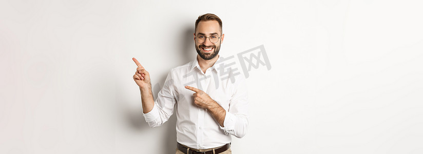 英俊的成功商人用手指指着右边，以高兴的脸、白色背景展示广告