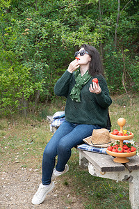 年轻漂亮的黑发女人在长凳上野餐时吃草莓甜点