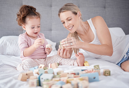 床、快乐的母亲和带着玩具的婴儿在家庭卧室里与字母教育积木一起玩耍。
