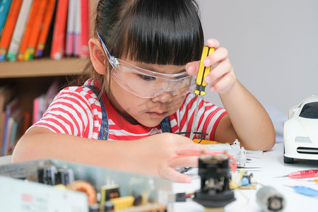 小女孩背景摄影照片_专注的小女孩用手中的工具修理她的玩具无人机，并用螺丝刀仔细组装玩具无人机。