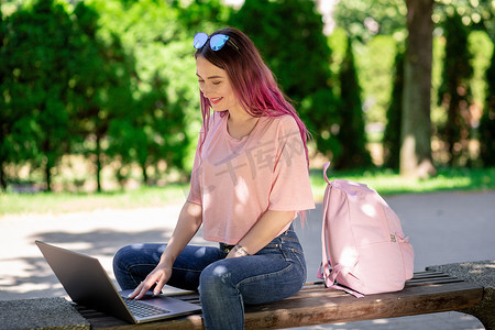 小女孩正在春天公园学习，坐在木凳上，在笔记本电脑上浏览