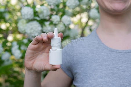 鼻腔喷雾剂摄影照片_幸福的女人在一棵开花的树的背景下展示鼻喷雾剂。