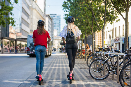 城市环境中时尚时尚少女骑公共租赁电动滑板车的后视图。