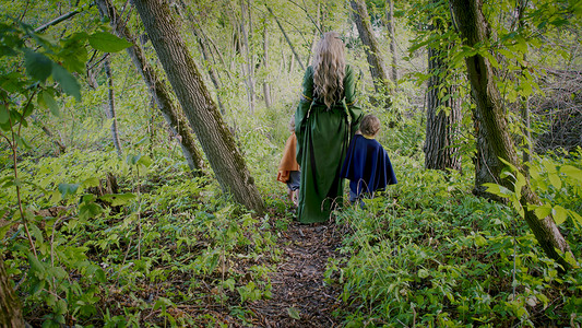 扮演了摄影照片_两个小男孩扮演侏儒或霍比特人和精灵女人在绿色森林中行走。