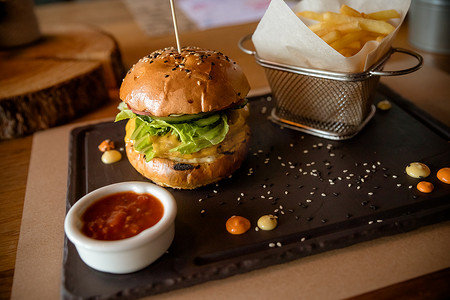 新鲜汉堡的特写镜头，石桌上放着一篮炸薯条，配上一碗番茄酱。美味、美味的牛肉汉堡，配有新鲜蔬菜、薯条和凉拌卷心菜